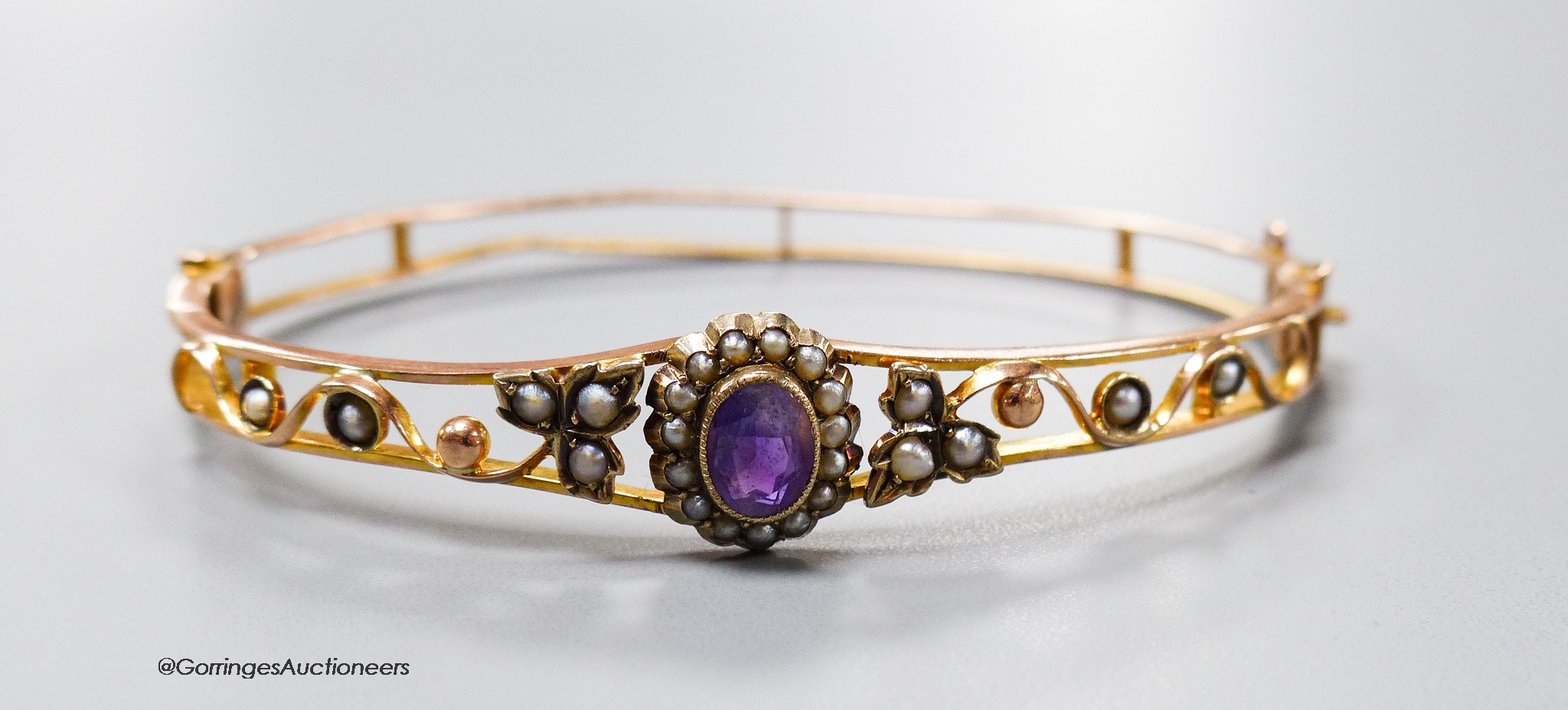 An Edwardian 9ct, amethyst and seed pearl cluster set hinged bracelet, interior diameter 61mm, gross 9.4 grams.